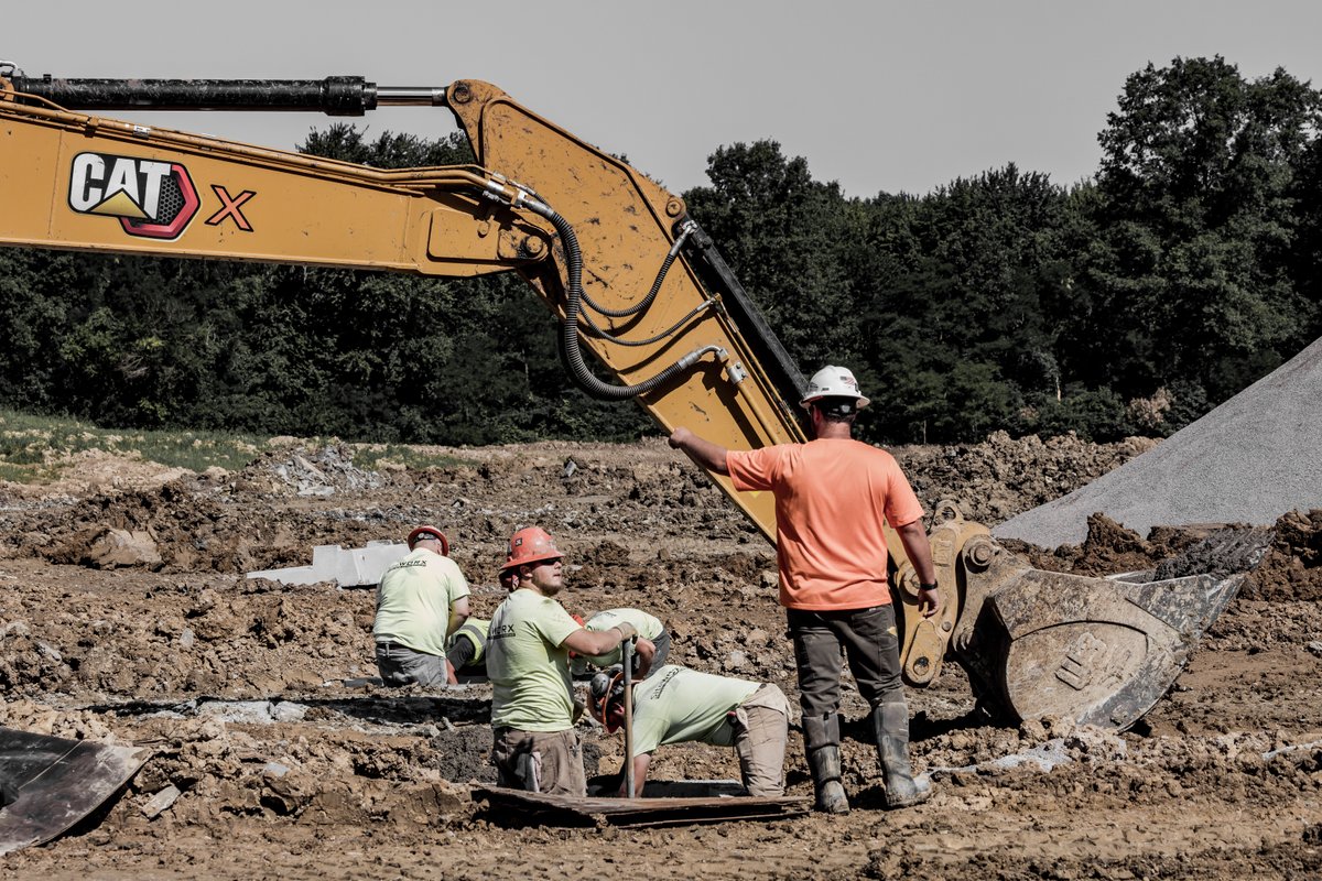 Construction workers in a hole next to construction equipment